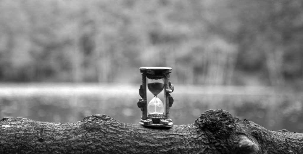 an hour glass sits on a log in greyscale